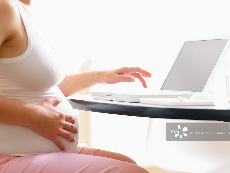 孕妇在餐桌上使用笔记本电脑，中段图片素材