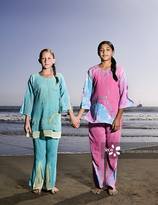 两个女孩(10-13)穿着纱丽在海滩，手牵手图片素材