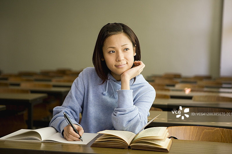 一位年轻女子坐在教室里，头靠着手写字图片素材