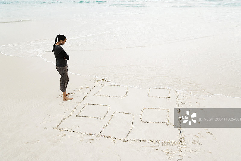 一名女子低头看着被沙滩上的沙子冲走的房子图片素材