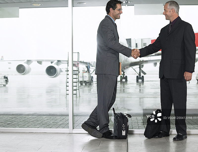 两个商人在机场互相问候，握手，微笑图片素材