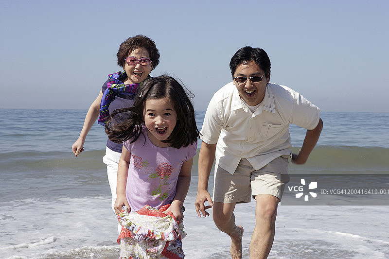 祖母，父亲和女儿(4-6)在海滩上跑步，面带微笑图片素材