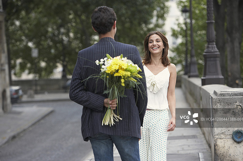 法国，巴黎，一对年轻夫妇在户外，男人背后拿着花图片素材