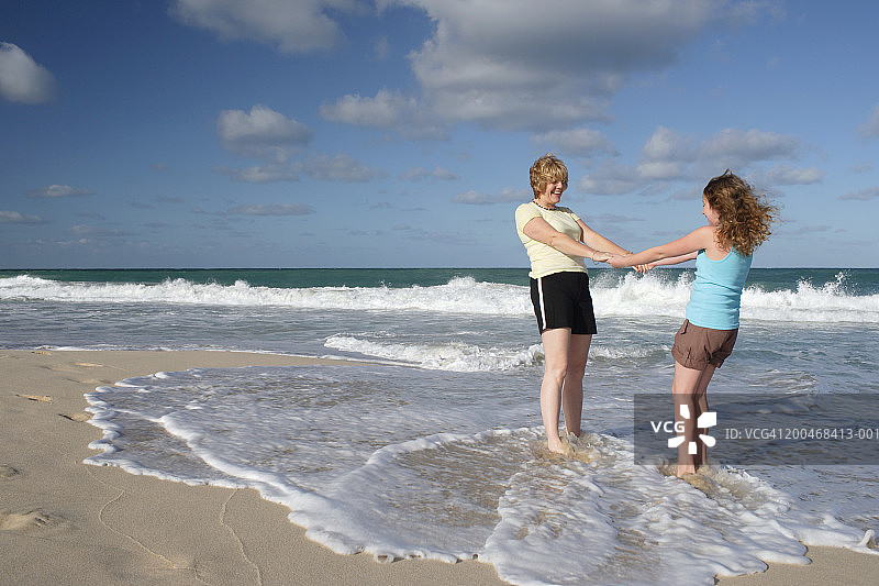 母亲和女儿手牵着手在沙滩上，微笑着，侧视图片素材