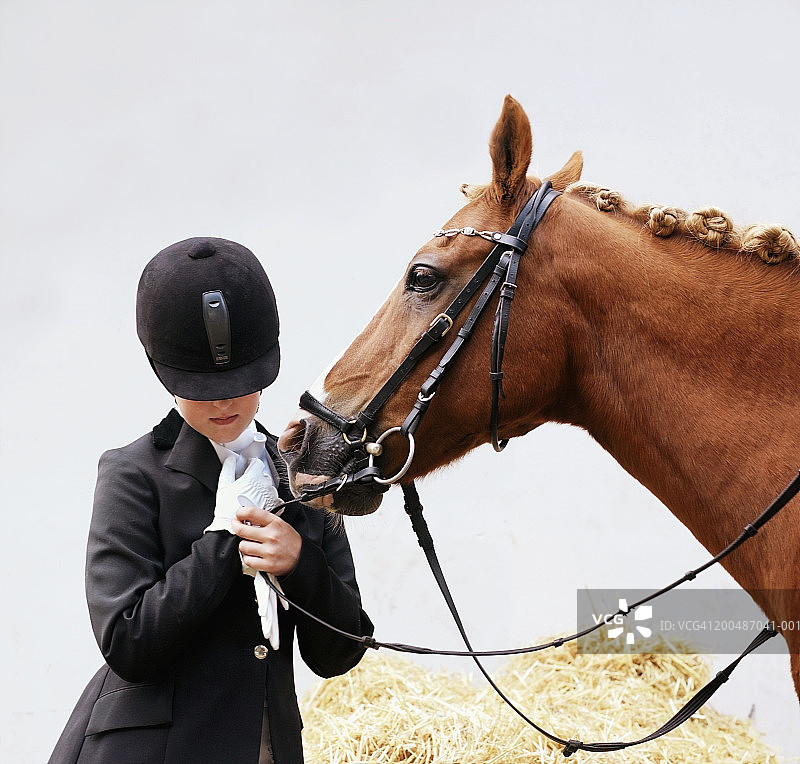 女孩(11-13)穿着骑马服站在马旁，握着缰绳图片素材