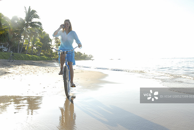 在海滩上骑自行车的时候用手机的女人图片素材