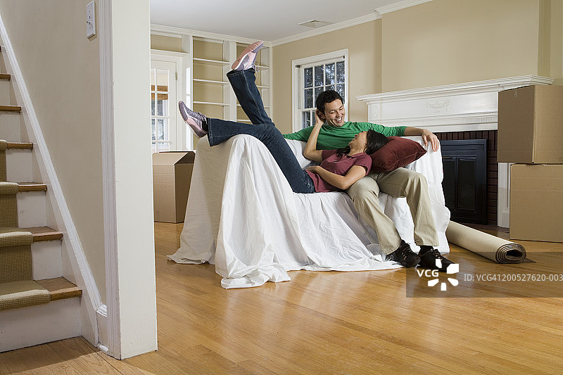 一对夫妇躺在客厅的有盖沙发上，上面放着纸箱，女人躺在男人的腿上图片素材