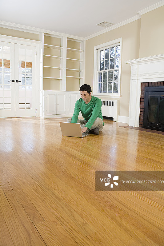 一名男子坐在空荡荡的客厅的抛光地板上，用着笔记本电脑图片素材