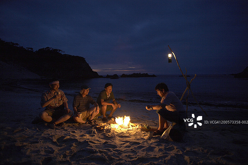 朋友们晚上在海滩上围坐在篝火旁图片素材