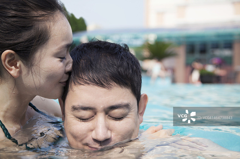 女人闭着眼睛在游泳池的水里亲吻男人的脸颊图片素材