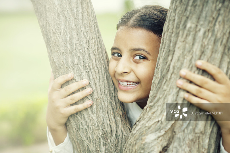 一个微笑的女孩从树上偷看的肖像图片素材