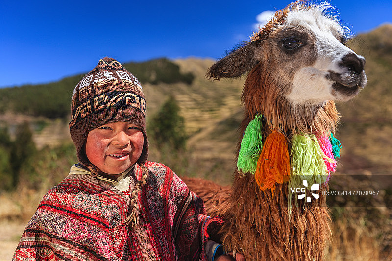 在库斯科附近，一个秘鲁小男孩穿着民族服装和美洲驼图片素材