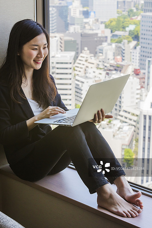 快乐年轻的日本现代女性坐在笔记本电脑图片素材