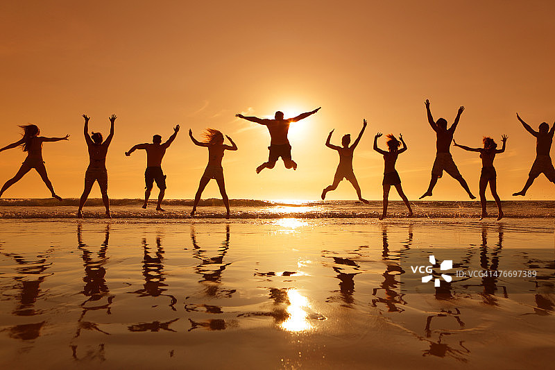 日落时分，年轻人在海滩上跳来跳去图片素材
