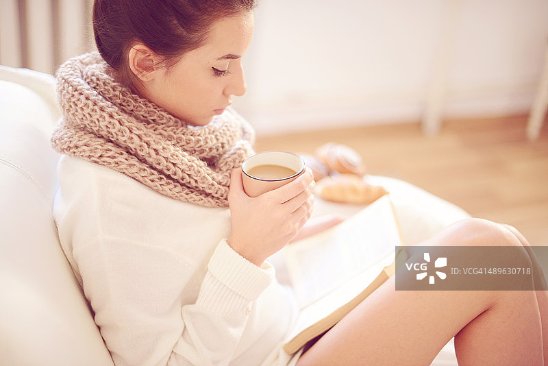 年轻漂亮的女人喝着热咖啡，读着书图片素材