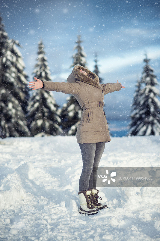 年轻女子在下雪的时候举起手臂享受冬天图片素材