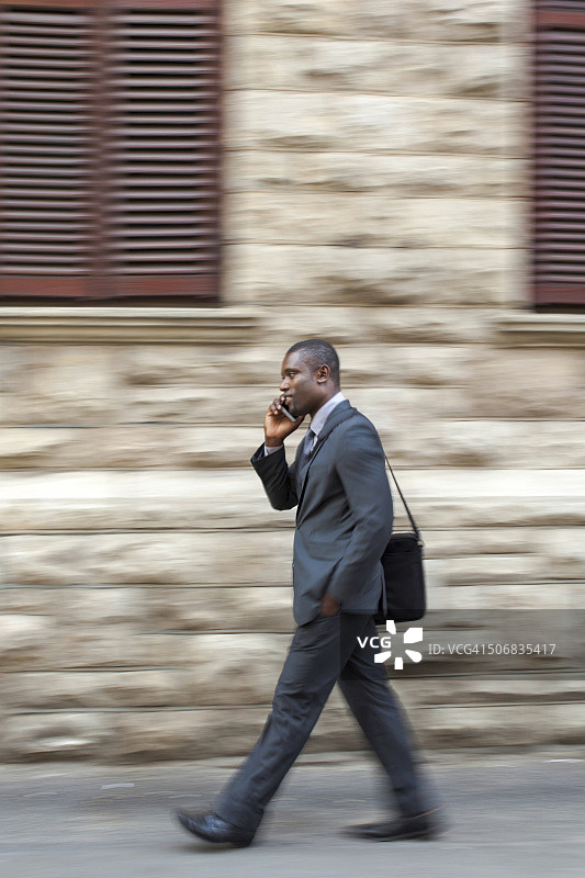 南非开普敦，一名非洲商人在市中心边走边用手机打电话图片素材