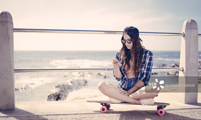 滑板女孩坐在滑板上看手机图片素材