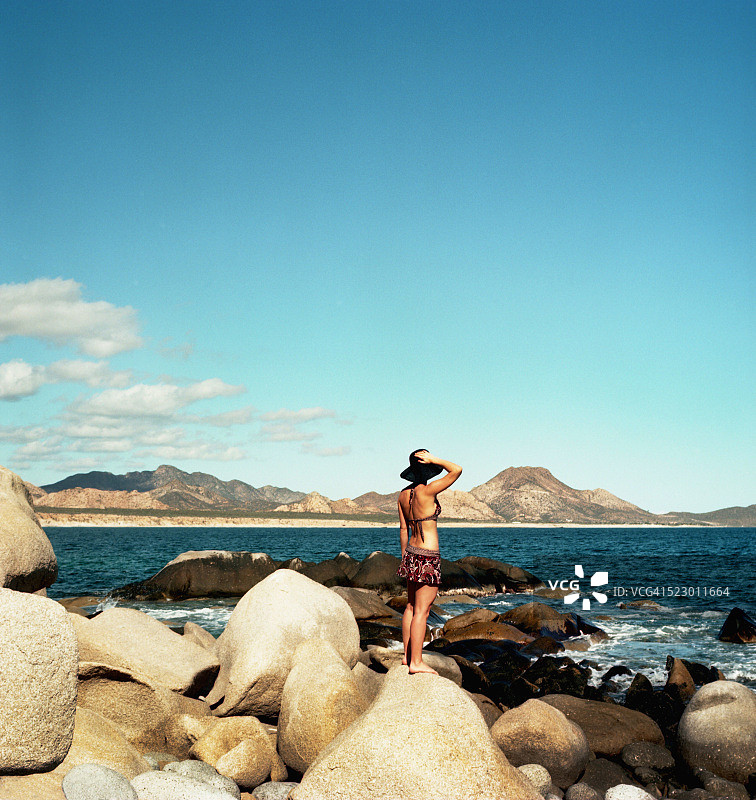 穿着泳衣的年轻女子站在巨石上俯瞰科尔特斯海图片素材