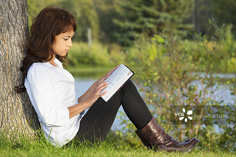 一个年轻女子在公园里读圣经图片素材