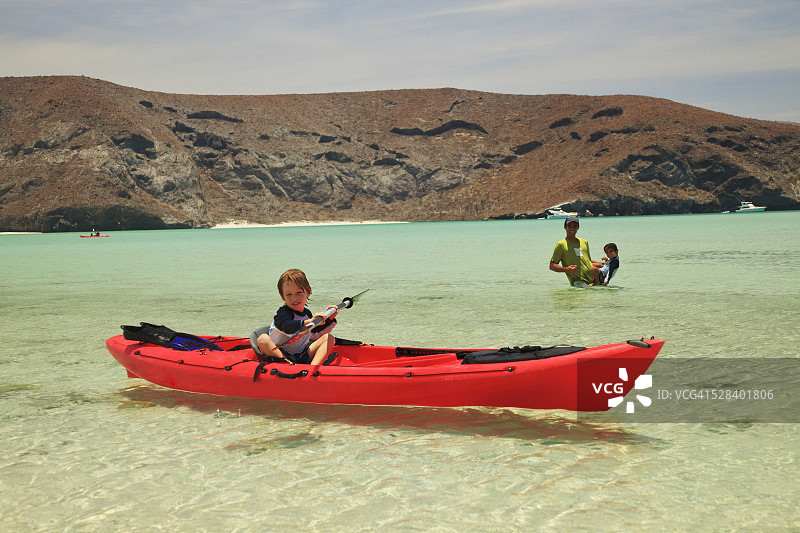 圣埃斯皮里图岛洛斯群岛国家海洋公园，一对父子在水里玩耍，一个小男孩坐在岸边的红船上;墨西哥下加利福尼亚的拉巴斯图片素材