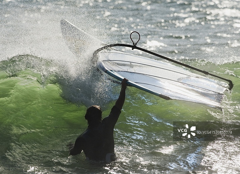 西班牙安达卢西亚加的斯的塔里法，一名男子在水里抓住他的风帆冲浪板图片素材