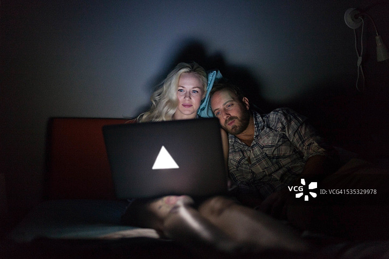 一对年轻夫妇在床上看笔记本电脑图片素材