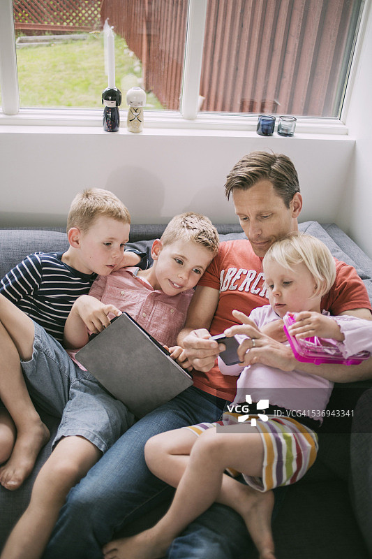 父亲和孩子在家里的沙发上使用科技产品图片素材