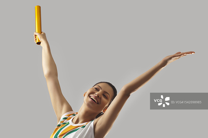 年轻的女运动员用接力棒庆祝胜利孤立在灰色的背景图片素材
