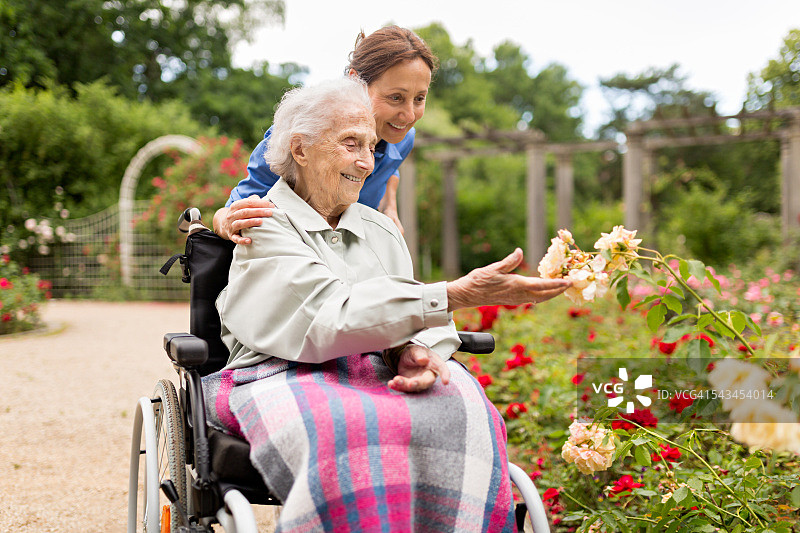 年长的妇女坐在轮椅上，由护工照顾图片素材