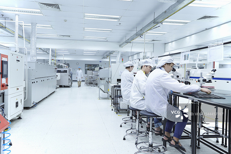 工人们在工厂里使用显微镜，专门在柔性表面上创建功能电路图片素材