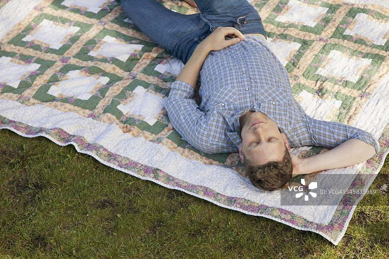 一个男人躺在公园的毯子上图片素材