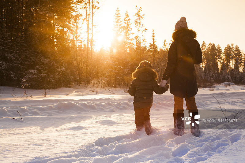 母子俩走在白雪覆盖的森林空地上图片素材