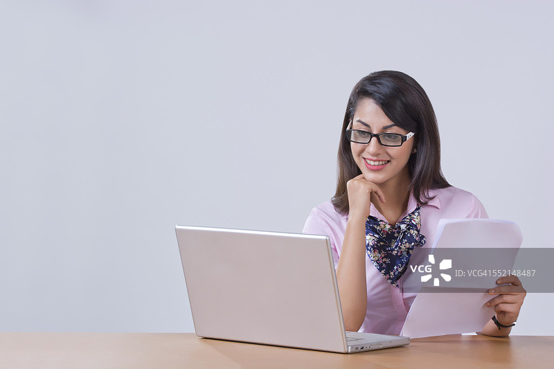 微笑的年轻女商人在办公桌上用笔记本电脑工作图片素材