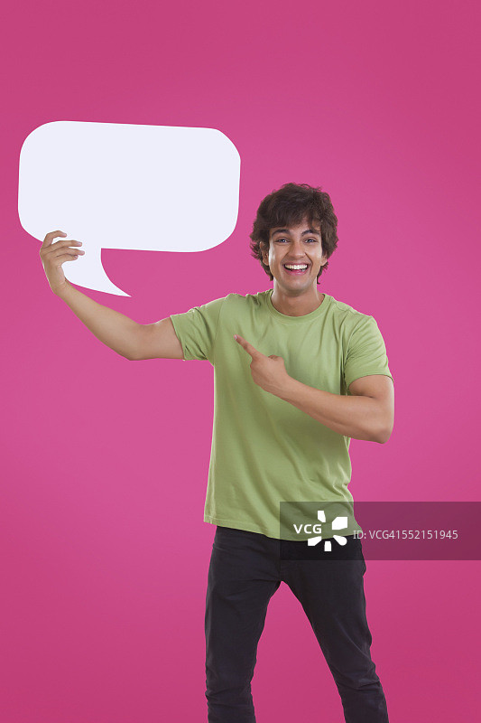 一个微笑的年轻人指着粉红色的背景上的语音泡泡图片素材