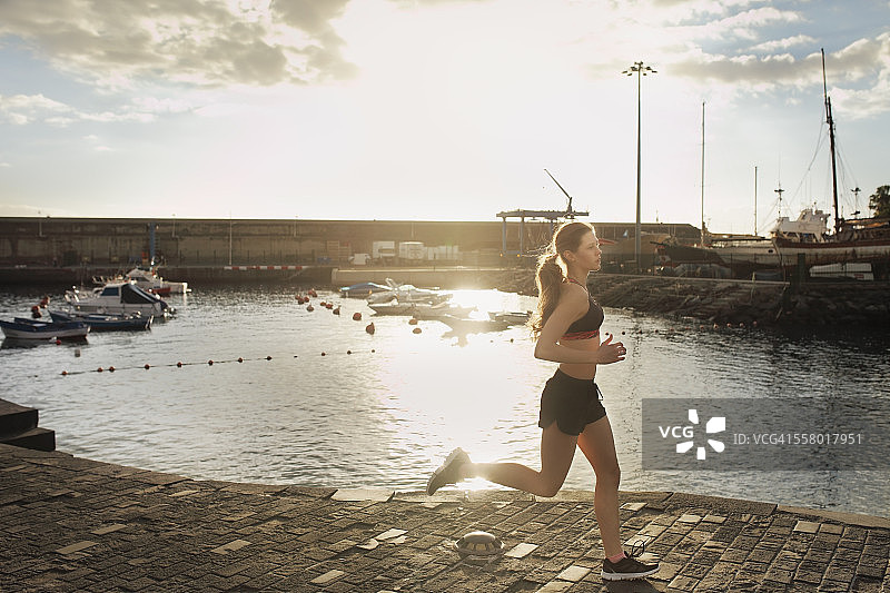 日落时分，一名女子在港口附近奔跑图片素材