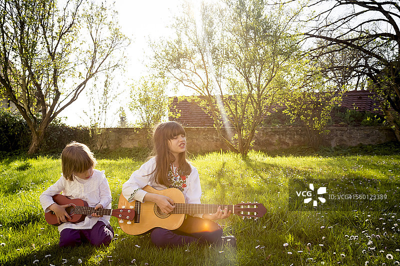 两姐妹坐在草地上弹吉他图片素材