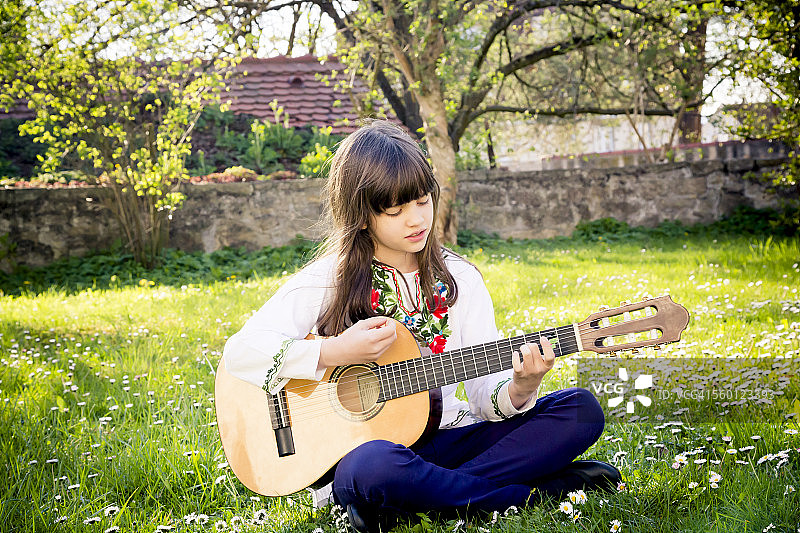 一个女孩坐在草地上弹吉他图片素材