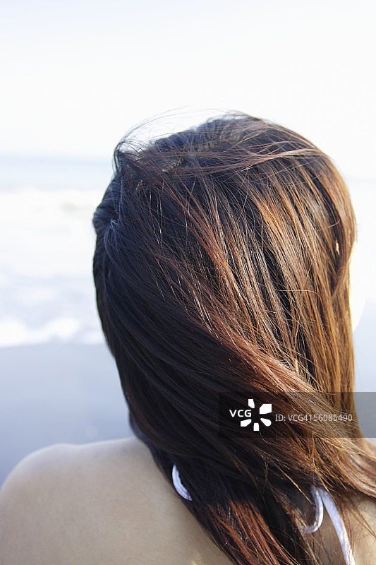 一个穿着比基尼的年轻女子坐在海滩上，后视图，特写图片素材