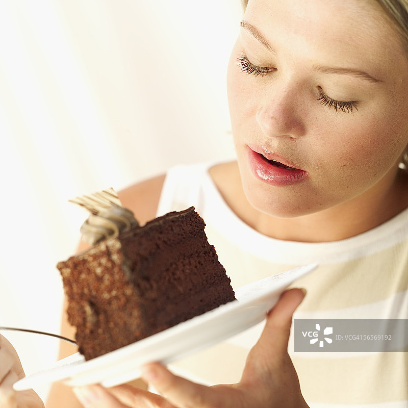 一个年轻的女人拿着一块巧克力蛋糕在盘子上的特写镜头图片素材
