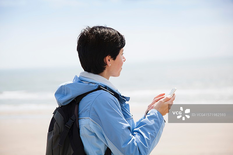 中年成年女子在海滩上发智能手机短信，同时看着大海图片素材
