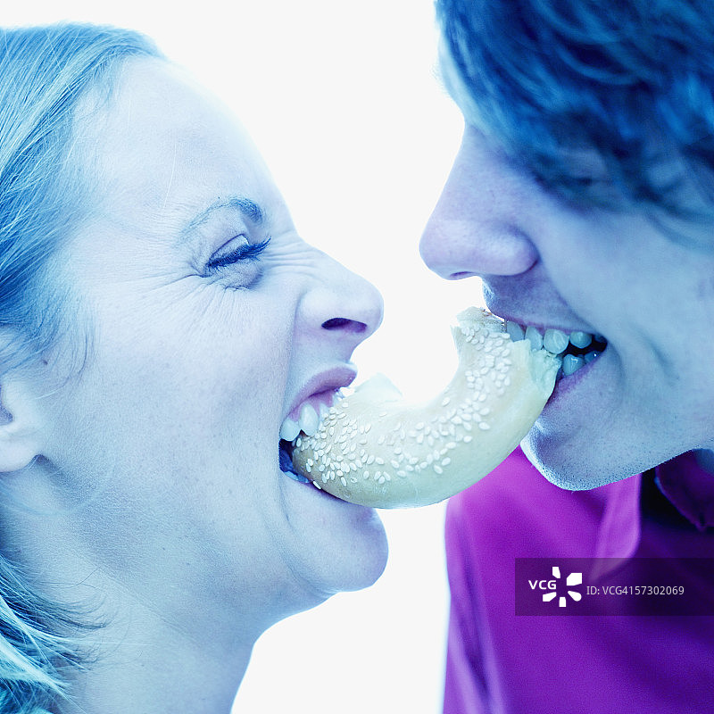 这是一对年轻夫妇的侧面照片，他们嘴里叼着半个百吉饼图片素材