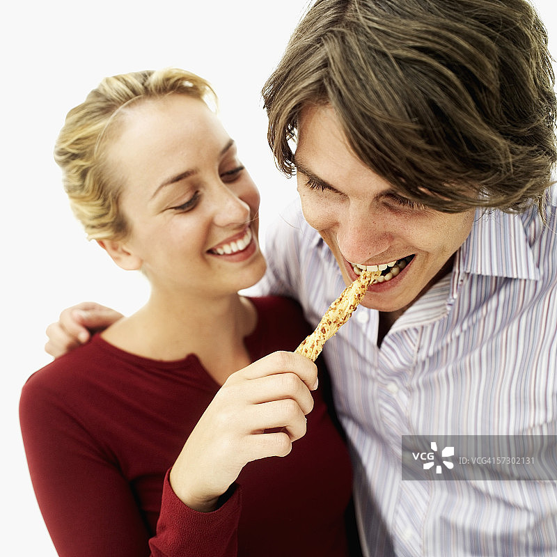 一个年轻女子喂一个年轻男子面包棒的特写镜头图片素材