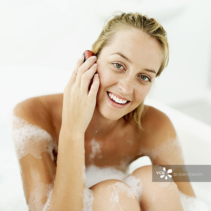 一个年轻女子在泡泡浴中打电话图片素材