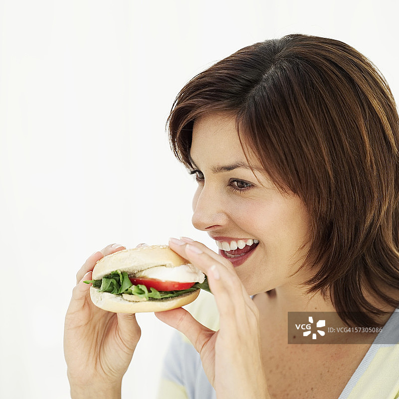 一个正在吃百吉饼三明治的年轻女人的侧影图片素材