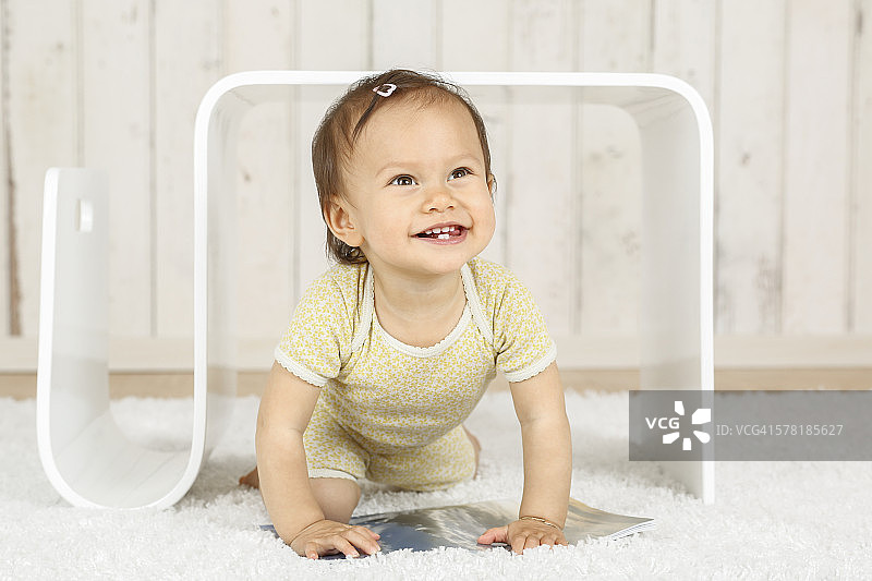 微笑的女婴蜷缩在现代边桌下的肖像图片素材