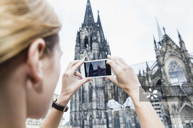 德国，科隆，一名年轻女子用智能手机拍摄科隆大教堂的照片图片素材