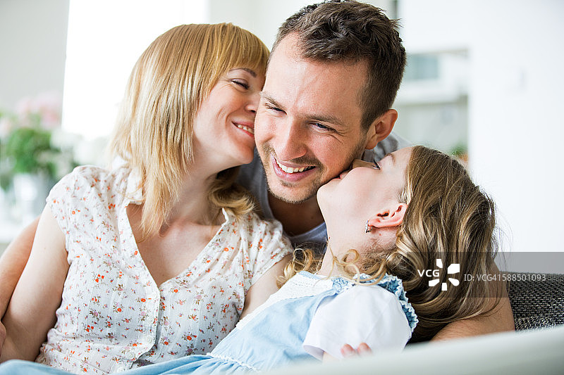 幸福的一家人坐在沙发上，妈妈和女儿亲吻爸爸图片素材