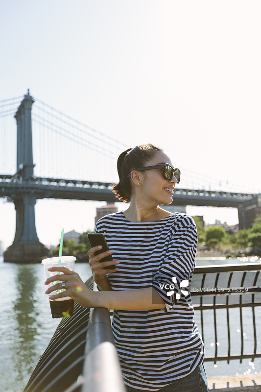 美国，纽约，年轻女子微笑着喝着软饮料看智能手机图片素材
