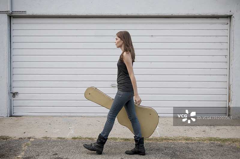 一个白人女人拿着吉他盒走在人行道上图片素材